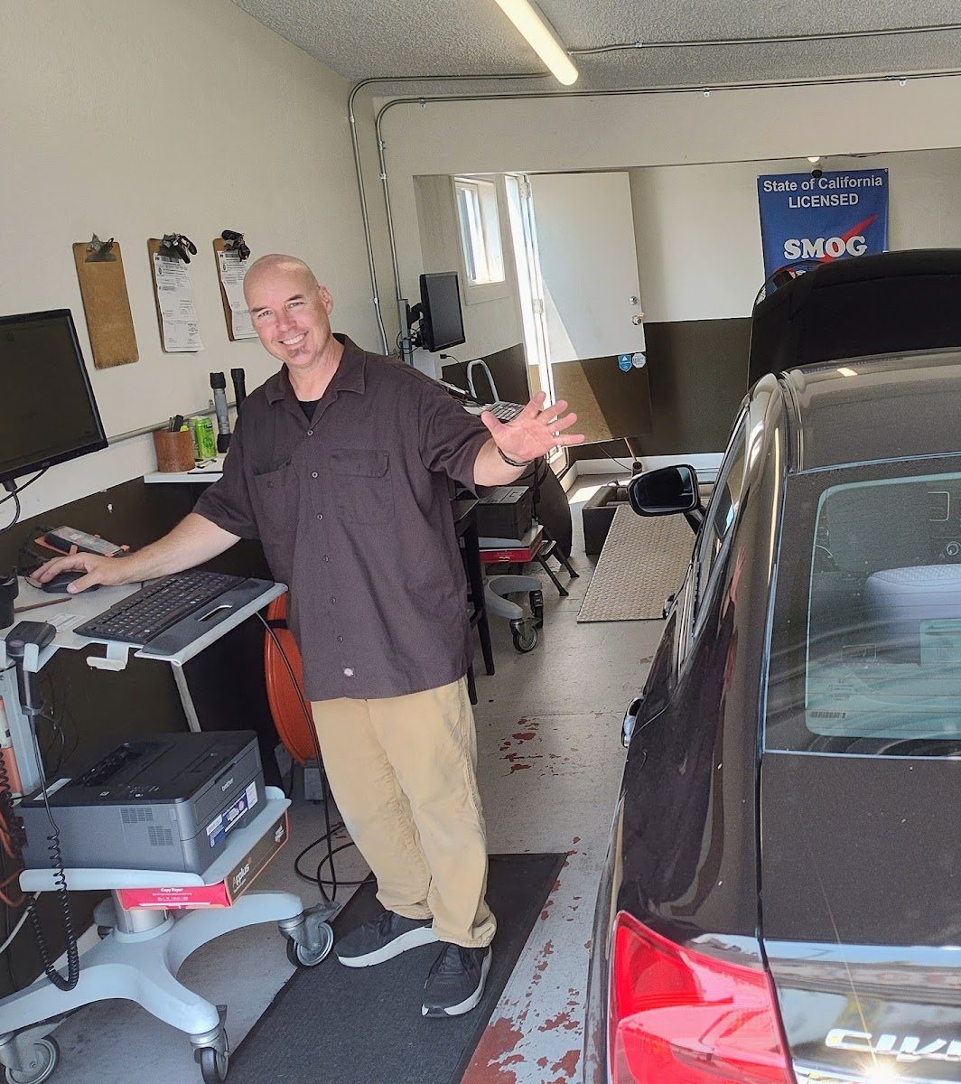 A Smog Oasis technician at the emissions test station beside a customer car